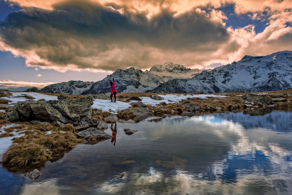 Person standing on rock near lake under cloudy sky