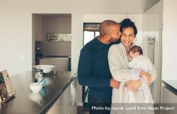 Man kissing his wife holding a newborn baby boy in kitchen 4dABab