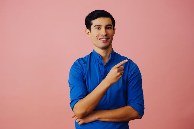 Medium shot of Latino man in pink studio with finger pointed up to the right
