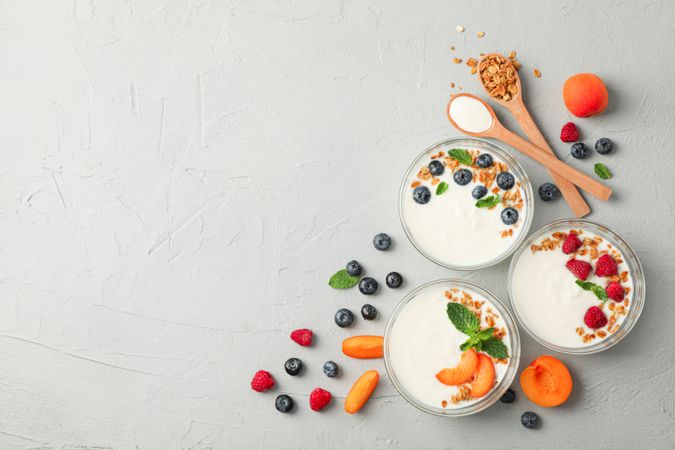 Flat lay composition with yogurt desserts and fruits on grey cement background