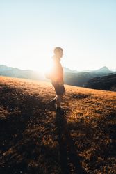 Side view of man in red jacket with backpack walking on shrubland at sunset