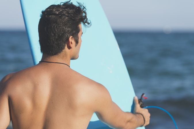Male surfer holding blue board standing in front of the sea