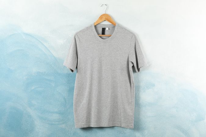 Hanger with blank gray t-shirt on blue background, space for text