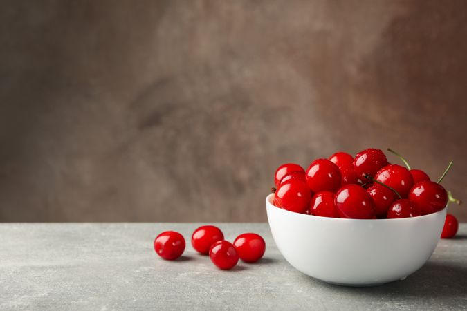 Bowl with red cherry on gray table, space for text