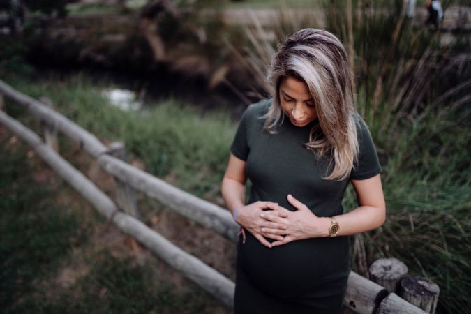 Happy pregnant woman standing at river in park