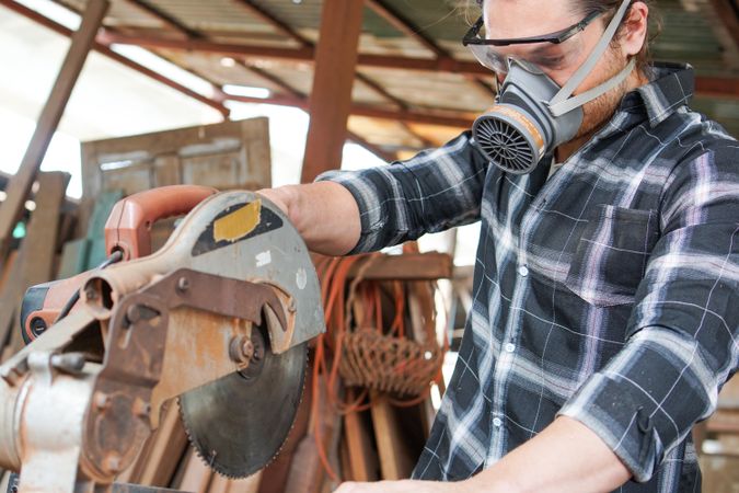 Male carpenter using electric circular saw cutting wood board in woodworking shop