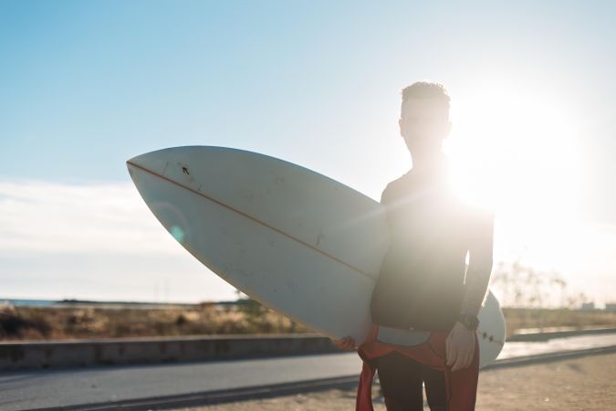 Backlit man standing on road with surfboard