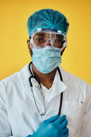 Closeup portrait of Black male doctor in yellow studio with full ppe gear ready for surgery