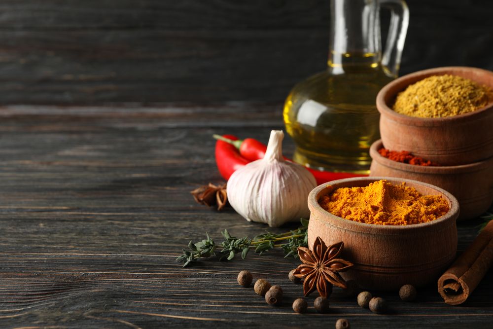 Turmeric in bowl with cinnamon sticks, garlic bulb and anise, copy space