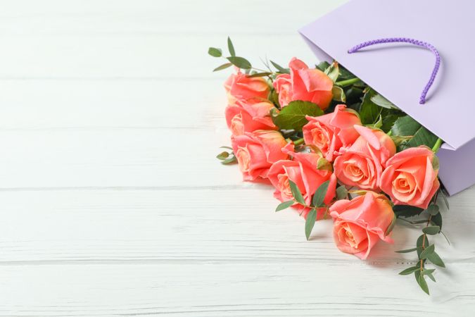 Gift bag with bouquet of pink roses on wooden background, space for text