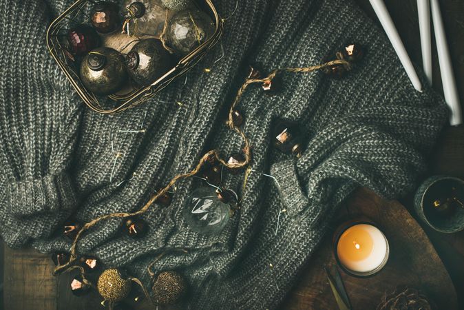 Festive decorations, candles and garland resting on grey woolen sweater