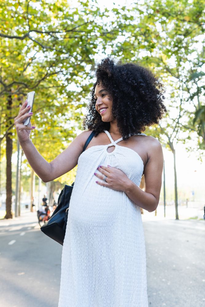 Smiling Black pregnant woman taking selfie on smartphone
