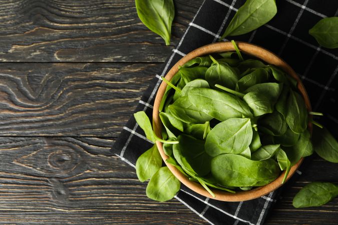 Wooden bowl with spinach and napkin on wooden background