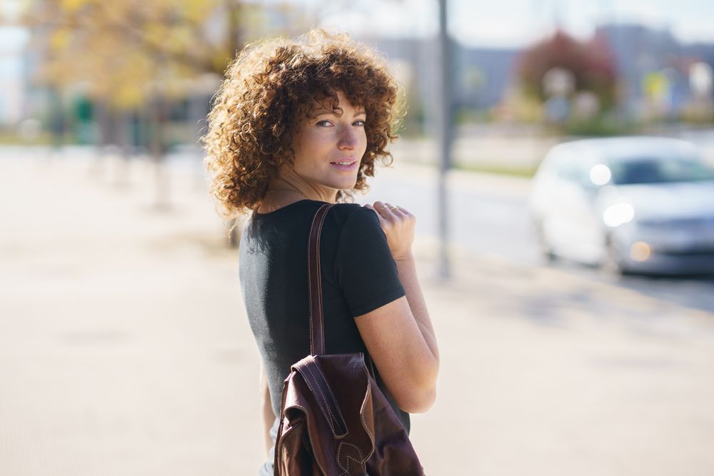 A young woman with beautiful curly hair is happily walking on a sunlit city street