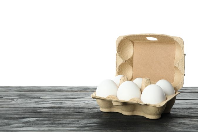 chicken eggs in carton box on wooden table isolated on plain background, space for text