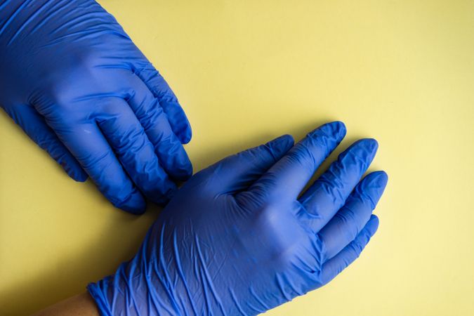 Top view of yellow table with hands wearing protective blue gloves