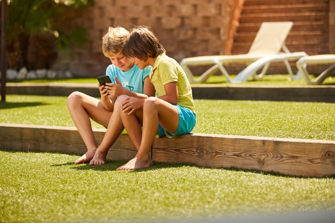 Cheerful boys browsing smartphone sitting on garden