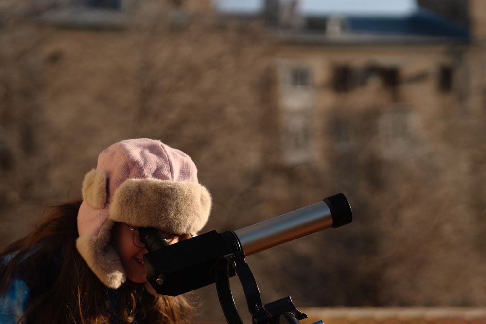 Girl in colorful jacket points while preparing solar telescope observation