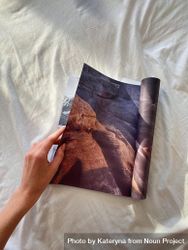 Hand leafing through a magazine on bedsheets 0Kea14