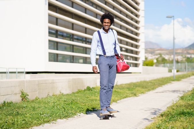 Smiling man with afro hair riding skateboard next to office