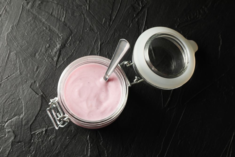 Glass jar with fruit yogurt on dark cement background, space for text