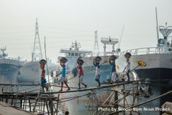 Group of people holding basins over their head walking from ship toward land 5oKo95