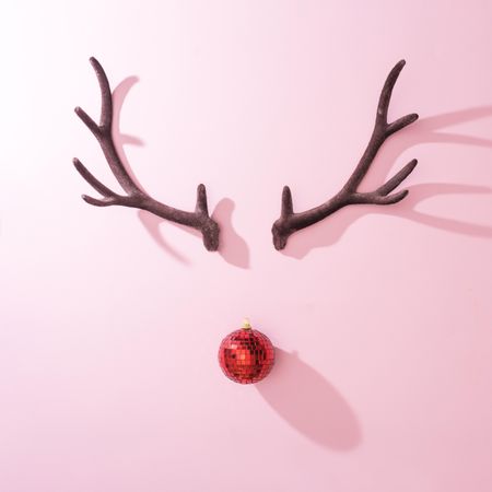 Red Christmas disco ball bauble with reindeer antlers on pink background with shadows