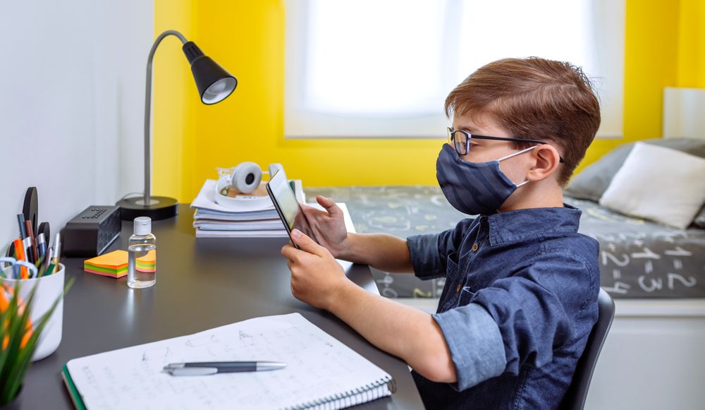 Boy with face mask doing homework with a tablet