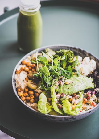 Healthy vegetarian bowl pictured on green surface with smoothie on side