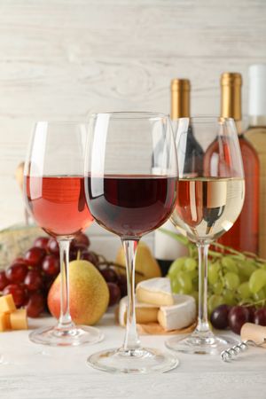 Fruits, cheese, bottles and glasses with different wine on light background, space for text