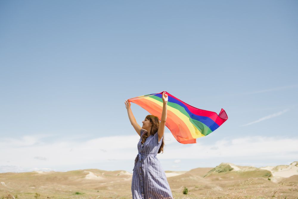 Young woman with rainbow banner against sky