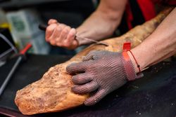 Close up of butcher’s hands holding ham and cutting with knife