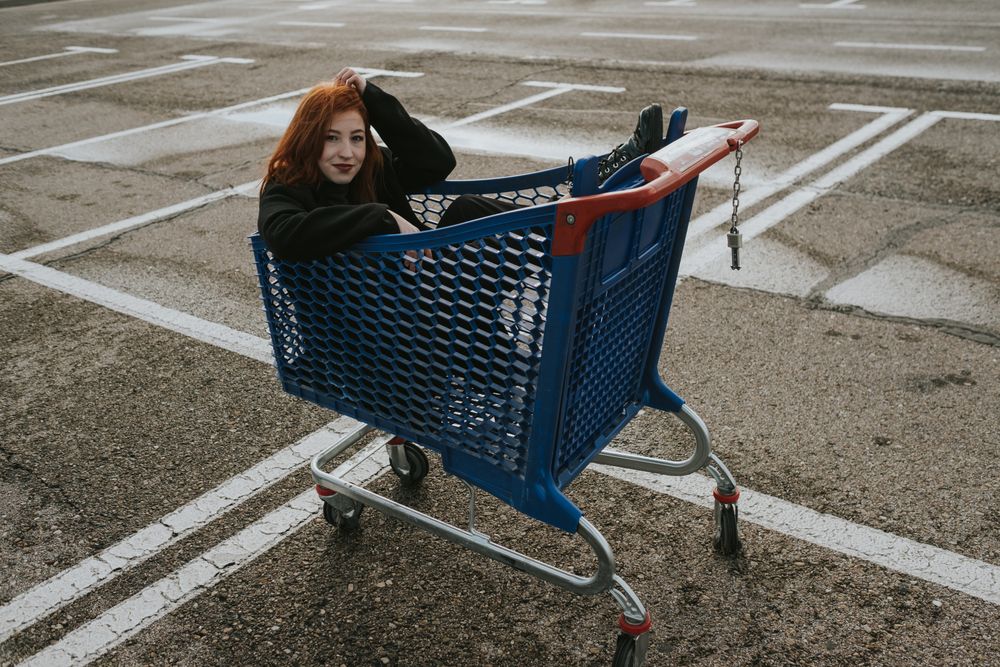 Smiling woman sitting in shopping trolley in parking lot