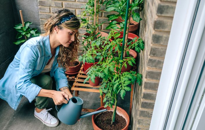Woman using watering can with plants of urban garden on terrace