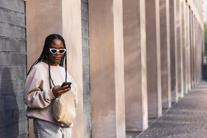 Black woman using smartphone near brick wall