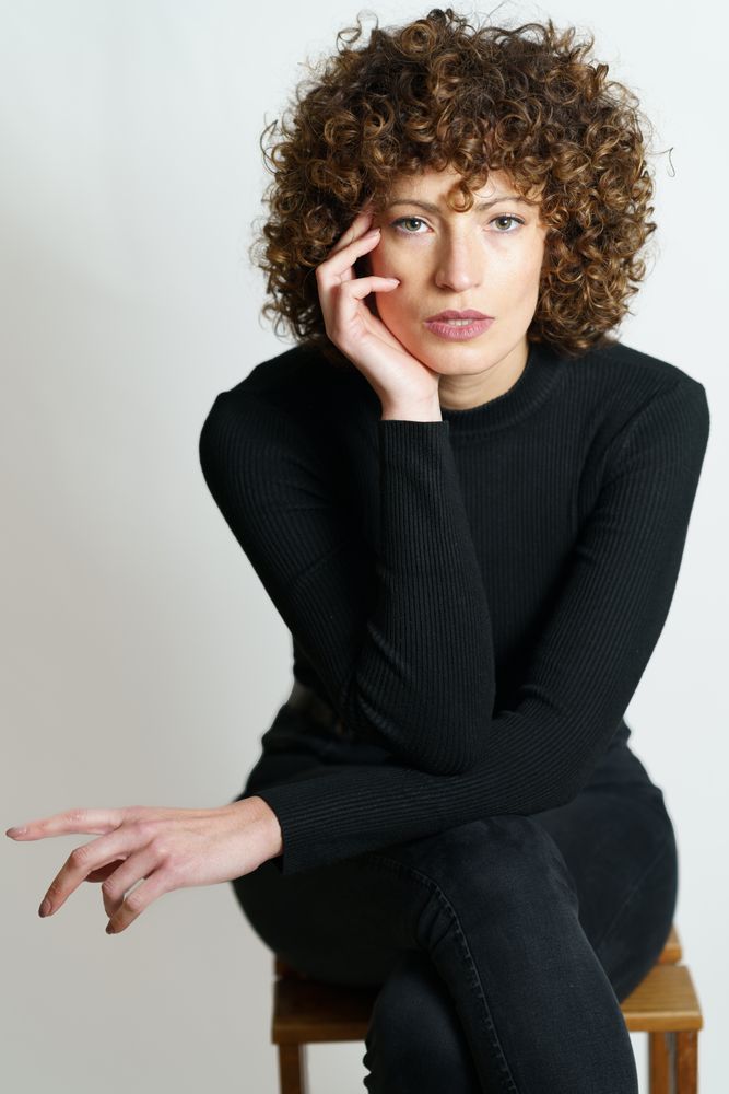Woman dressed in dark sweater and looking at camera resting head on hand
