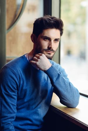 Contemplative man in sweater sitting in window of cafe