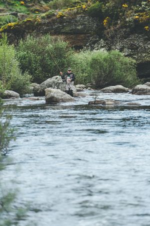 Confident man fishing with rod while standing in river stream