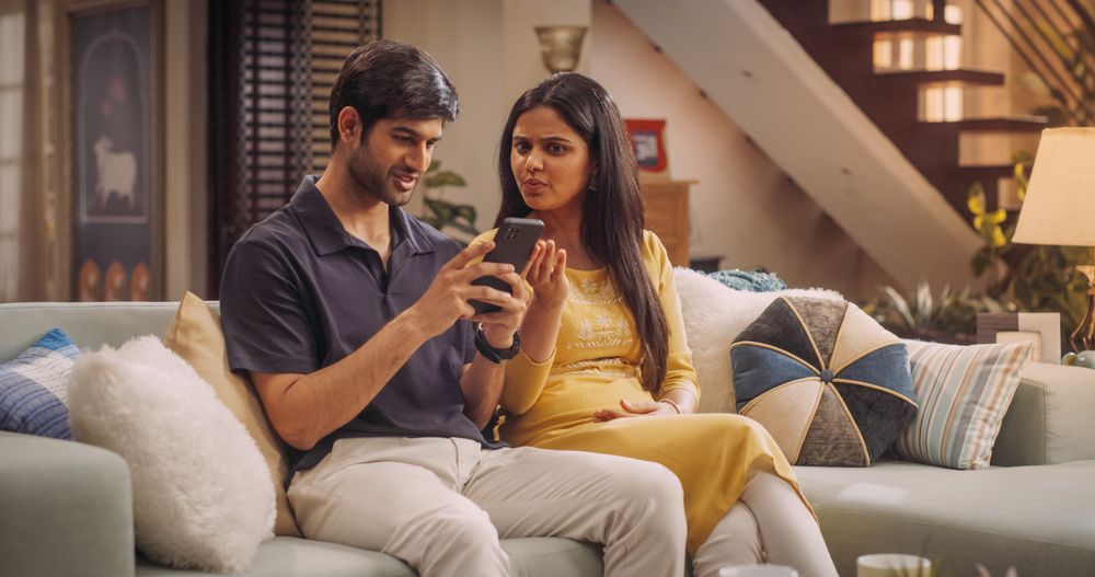 Young Indian Couple Using Internet On Smartphone, Sitting On The Sofa at Home