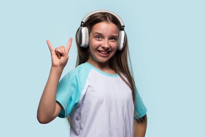 Excited girl making rock hand gesture while wearing headphones.