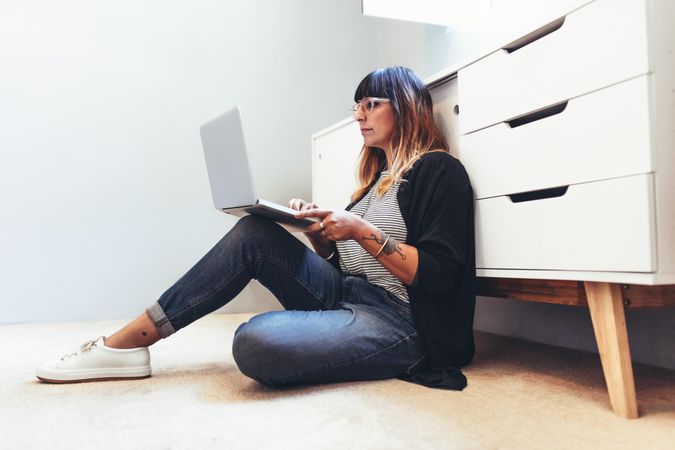 Freelance woman working on laptop computer sitting on floor