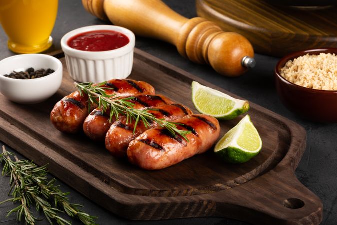 Grilled sausages on board with condiments, sides and lime slices