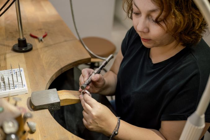 Focused adult craftswoman working in jewelry atelier