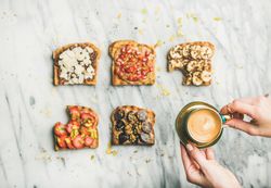 Toast topped with fresh fruit on marble background with hands lifting coffee, horizontal composition