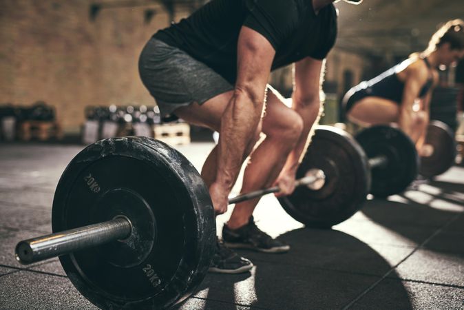 Crop shot of muscular male bending down to lift heavy barbell