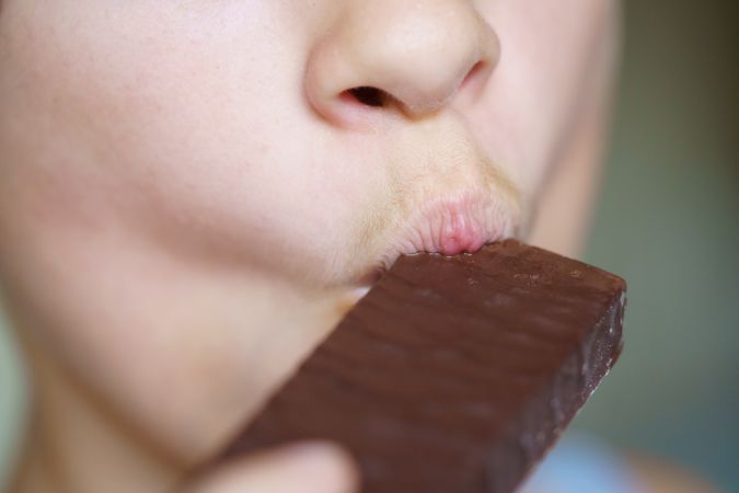 Mouth of girl biting into chocolate bar