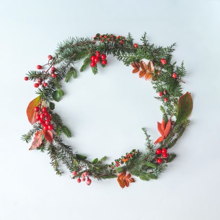 Winter leaves and berries in wreath on light background