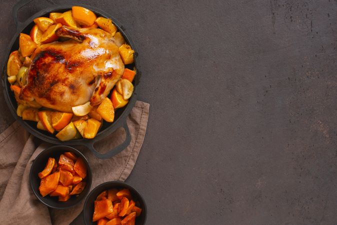 Chicken roasted in pot with oranges on table with copy space