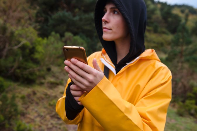 Woman in hoodie and yellow raincoat browsing smartphone