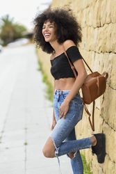Joyful female standing on street with one leg up leaning on wall